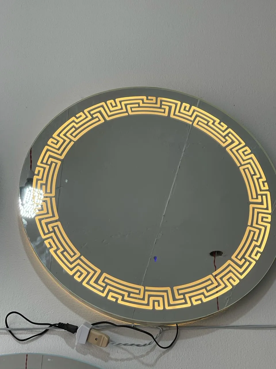 Warm golden illuminated Greek Key border round LED mirror mounted on wall in Sialkot